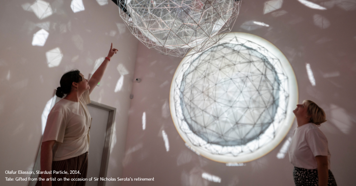Two woman stood under a silver and white light art circular artwork inside the Light Durham.